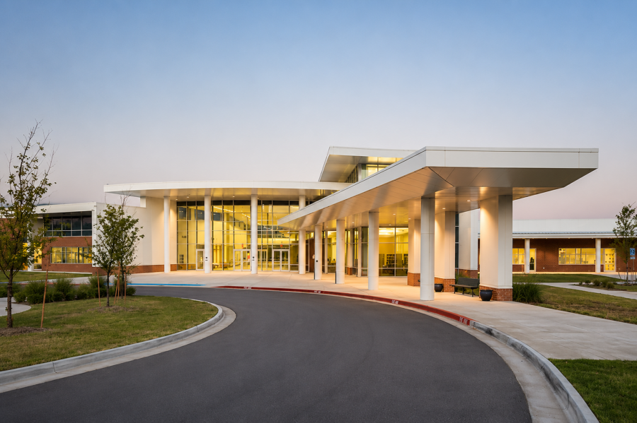 Sylvan Hills Middle School exterior at dusk in Little Rock, Arkansas, featuring the covered entrance, curved drop-off drive and glass-fronted lobby designed by WDD Architects.