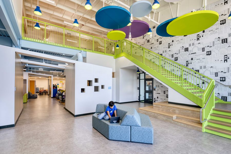 Jim Rollins Elementary School learning commons in Springdale, AR, featuring a bright green staircase, colorful suspended acoustic panels and flexible student seating.