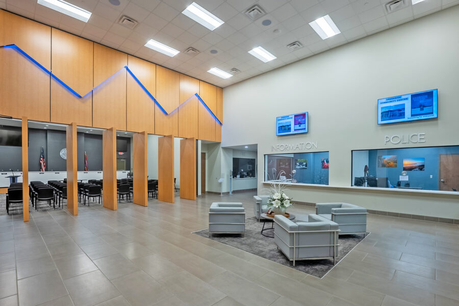 Municipal building lobby featuring a double-height public service area, wood wall panels, information and police service windows, and an adjacent meeting room, designed by WDD Architects.