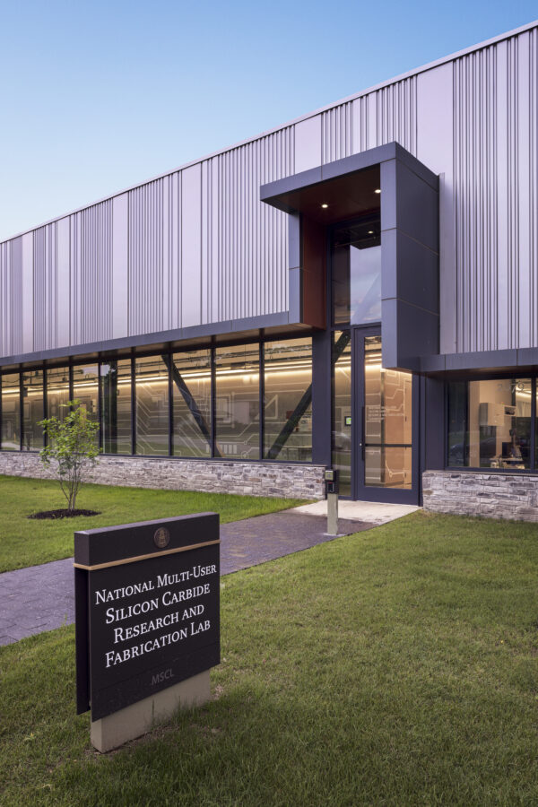Exterior entrance of the National Multi-User Silicon Carbide Research and Fabrication Lab (MUSiC) facility in Fayetteville, AR, featuring corrugated metal siding and glass entryway, designed by WDD Architects.
