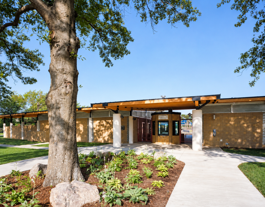 Exterior of the Springdale Aquatic Complex designed by WDD Architects, featuring tan masonry walls, a covered entrance, landscaped planting beds and pedestrian walkways.